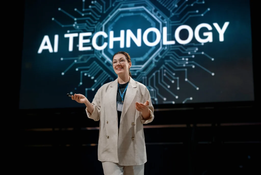 Mulher branca sorridente de óculos, palestrando feliz com um telão azul atrás dela representando Tecnologia de IA.